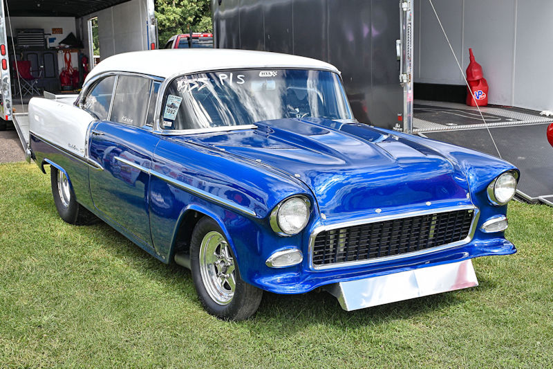 Classic blue 1955 Chevrolet Bel Air parked on grass, showcasing white roof and chrome details.