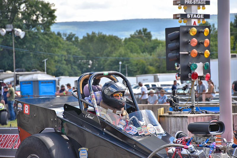 A drag racer in a race car waits at the starting line, with a traffic light signaling the start of the race in the background.