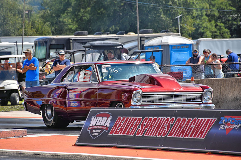 A vintage red car ready to race at Beaver Springs Dragway, with spectators watching in the background.