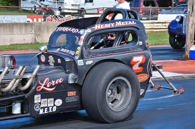 A classic drag racing car with a prominent '2' on the side, showcasing an array of stickers and a large rear tire, ready for a race.
