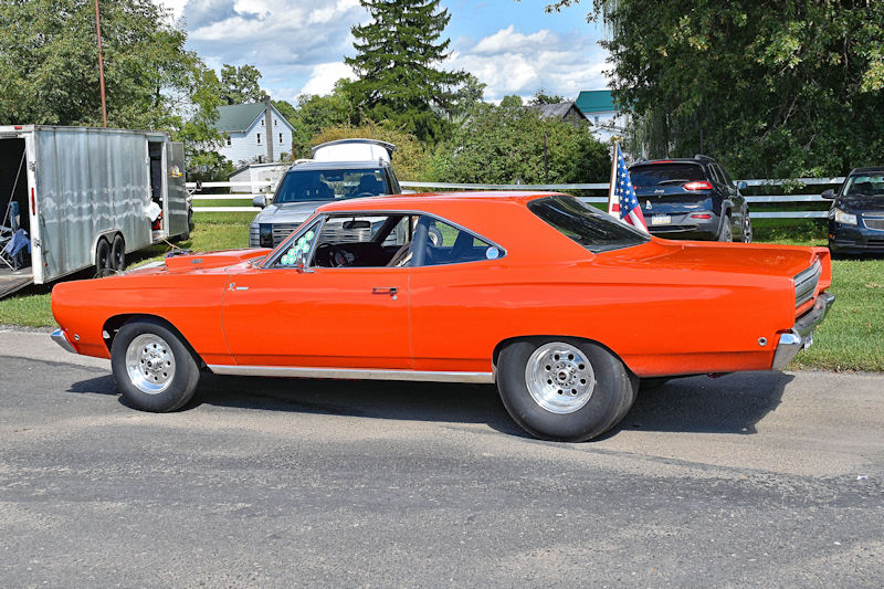 Bright orange vintage muscle car parked on a street, featuring a sleek design and large rear wheels.