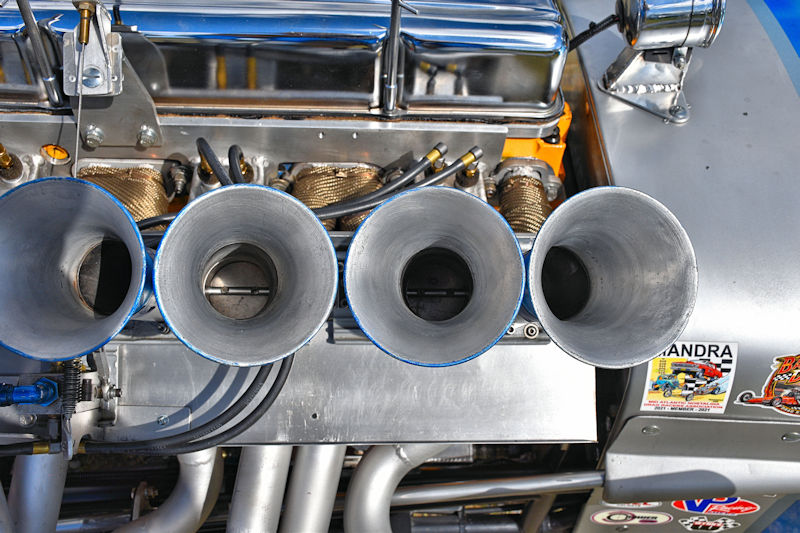 Close-up view of four metallic intake funnels on a racing engine, showcasing intricate details of the engine components.