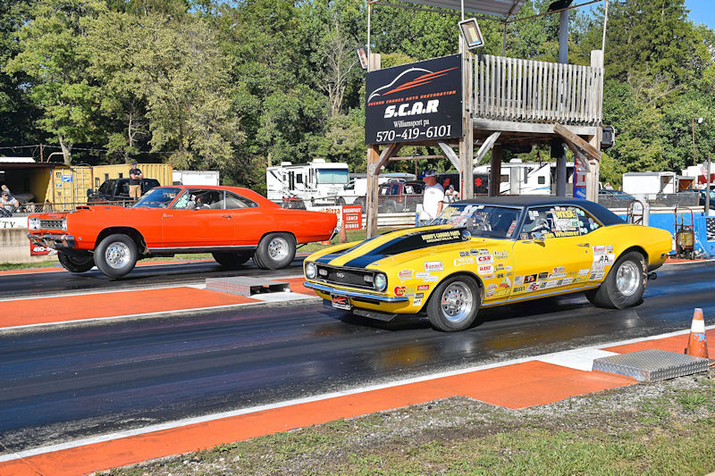 Two race cars on a drag strip, one red and one yellow with black stripes, preparing for a race.