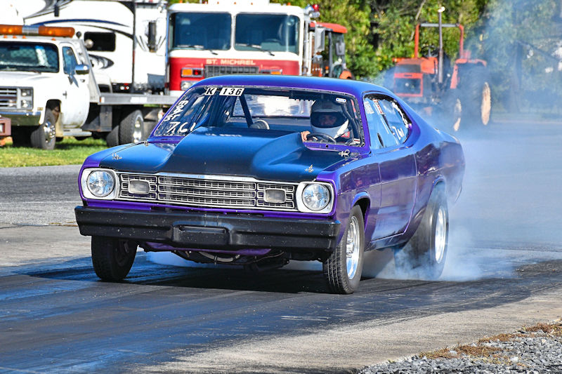 A purple and black modified car racing down a drag strip, leaving a trail of smoke behind.