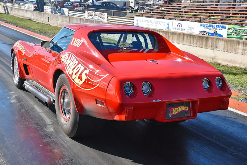 Rear view of a bright red racing car with 'Hot Wheels' graphics, positioned on a drag racing track.