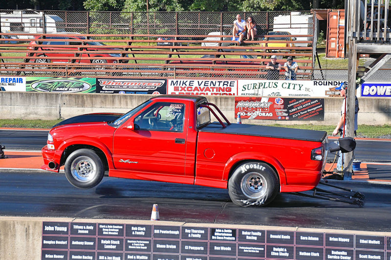 A red pickup truck in the process of taking off on a drag racing track, with its front wheels lifted off the ground.