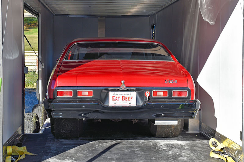 A red car with a license plate that reads 'EAT BEEF' is parked inside a trailer, viewed from the rear.