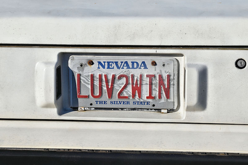 A close-up of a Nevada license plate featuring the text 'LUV2WIN' with a white background and some wear and tear.