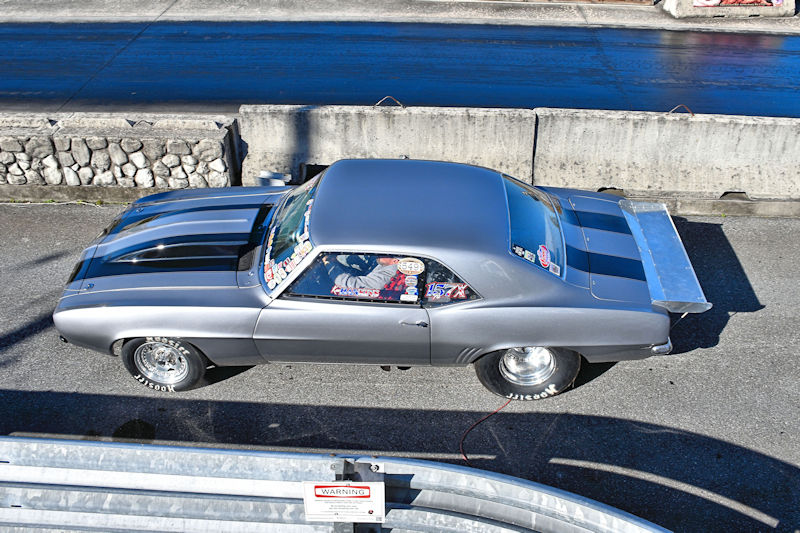 A sleek, gray muscle car with a large rear wing parked on a racing track, showcasing its stylish design and modifications.