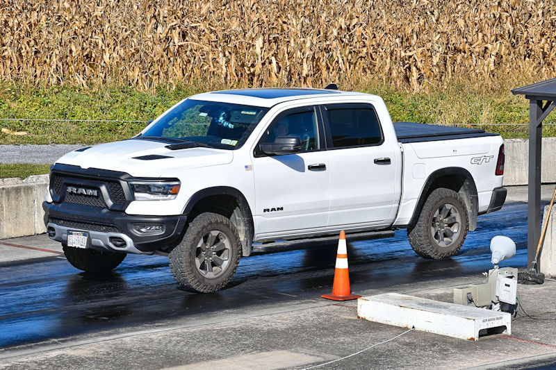 A white RAM truck parked on a drag strip, with cornfields in the background.