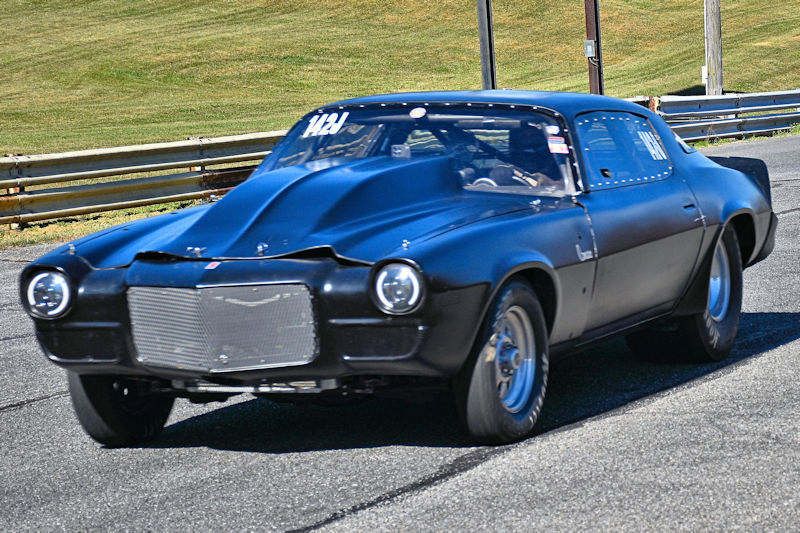 A black vintage race car with a sleek design, speeding on a racetrack with green grass in the background.