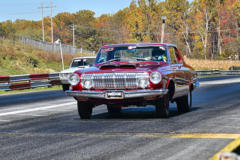 A classic red car racing on a drag strip with autumn foliage in the background.