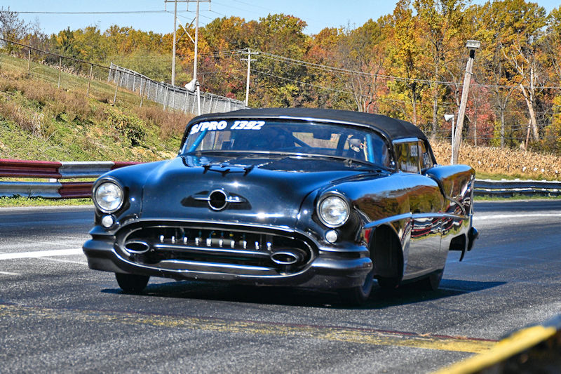A classic black car racing down a track, featuring a vintage design with a shiny finish and prominent front grille.