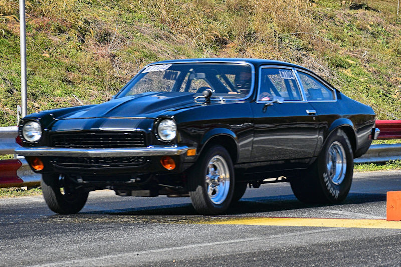 A classic black muscle car racing on a track, featuring chrome wheels and a sleek design.