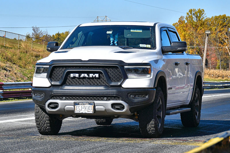 A white RAM truck parked on a roadway with autumn foliage in the background.