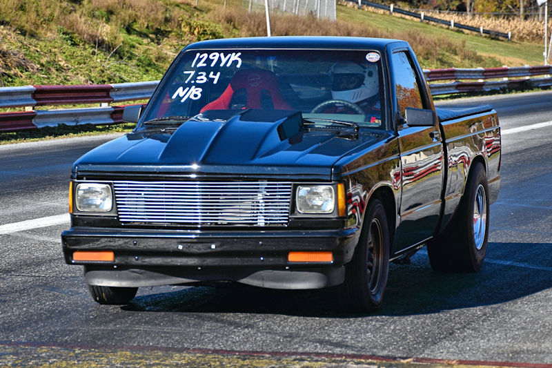 Black pickup truck on a racetrack, featuring a detailed hood and racing seat, with performance timings displayed on the windshield.