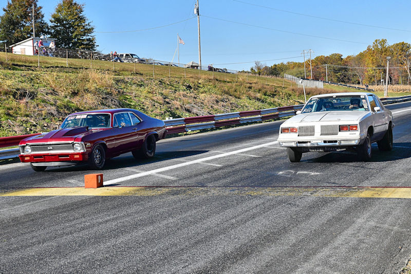 Two classic cars racing on a drag strip under clear blue skies.