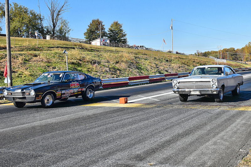 Two classic cars lined up at a drag racing track, ready to race against each other.