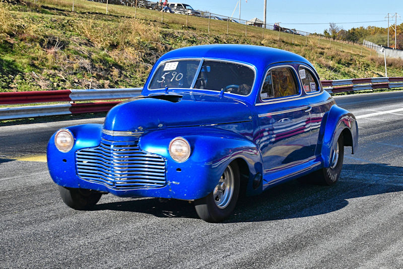 A vintage blue car racing down a track, showcasing its classic design and shiny finish.