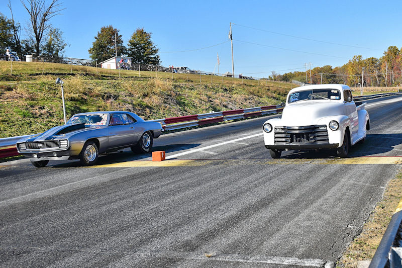 Two classic cars positioned at the start line of a drag racing track, ready for a race on a sunny day.