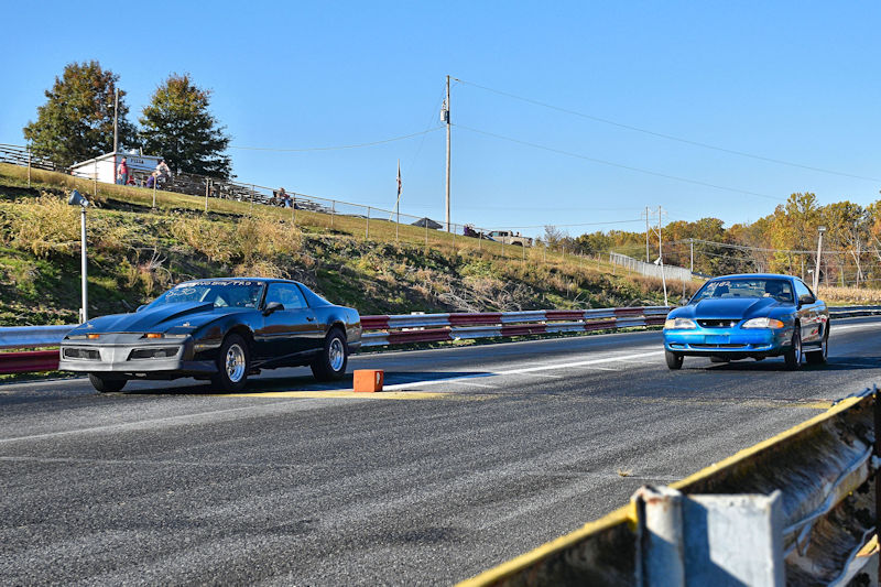 Two race cars competing on a drag strip with a clear blue sky in the background.