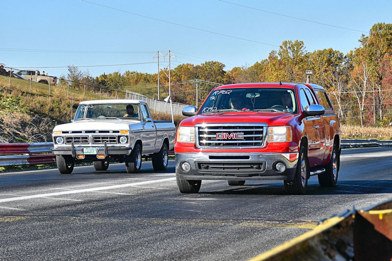Two trucks racing on a strip, a white vintage truck on the left and a red GMC truck on the right.
