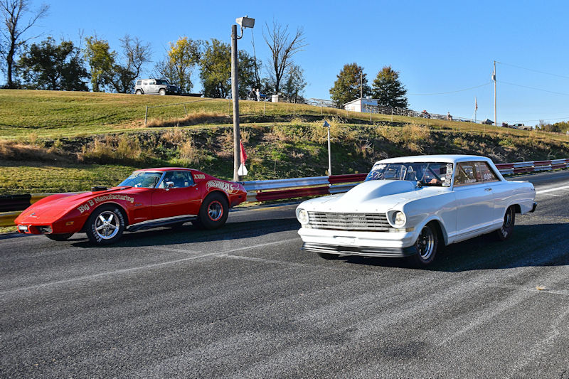 A red sports car and a white classic car racing on a drag strip with a grassy background.