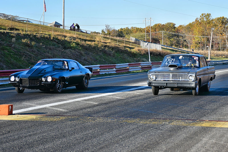 Two classic cars racing on a drag strip during a sunny day.