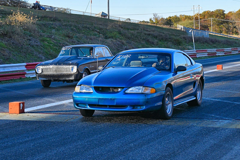 A blue sports car and a black classic car racing on a drag strip.