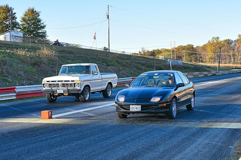 A white pickup truck and a black sports car racing down a drag strip.