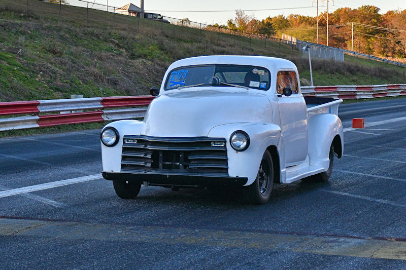 A vintage white pickup truck with black wheels, positioned on a racetrack, showcasing a classic design.