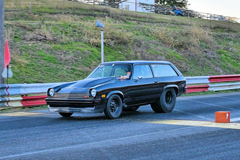 A black car accelerating on a drag strip, featuring large rear tires and a sleek design.